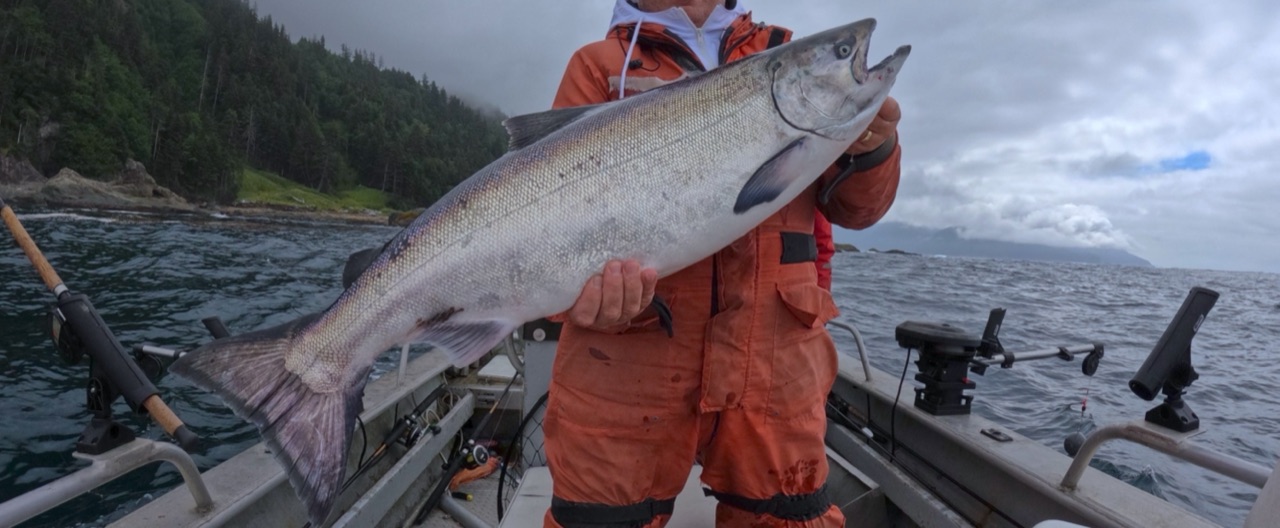 Two anglers in rain gear holding a large Pacific salmon on a boat in coastal waters